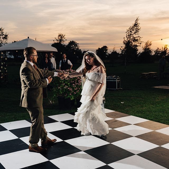 A bride and groom exchange vows on a black and white checkered dance floor at an outdoor evening wedding ceremony.