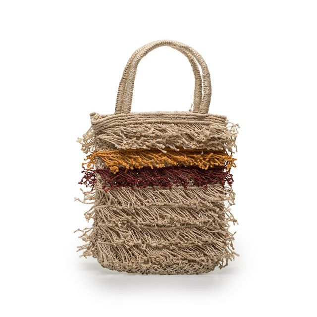 A woven straw tote bag with horizontal stripes in natural, gold, burgundy and tan colours, featuring frayed edges and handles.
