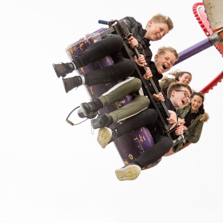 A group of children on a fairground ride, laughing and holding onto a central pole as the purple ride spins them around.