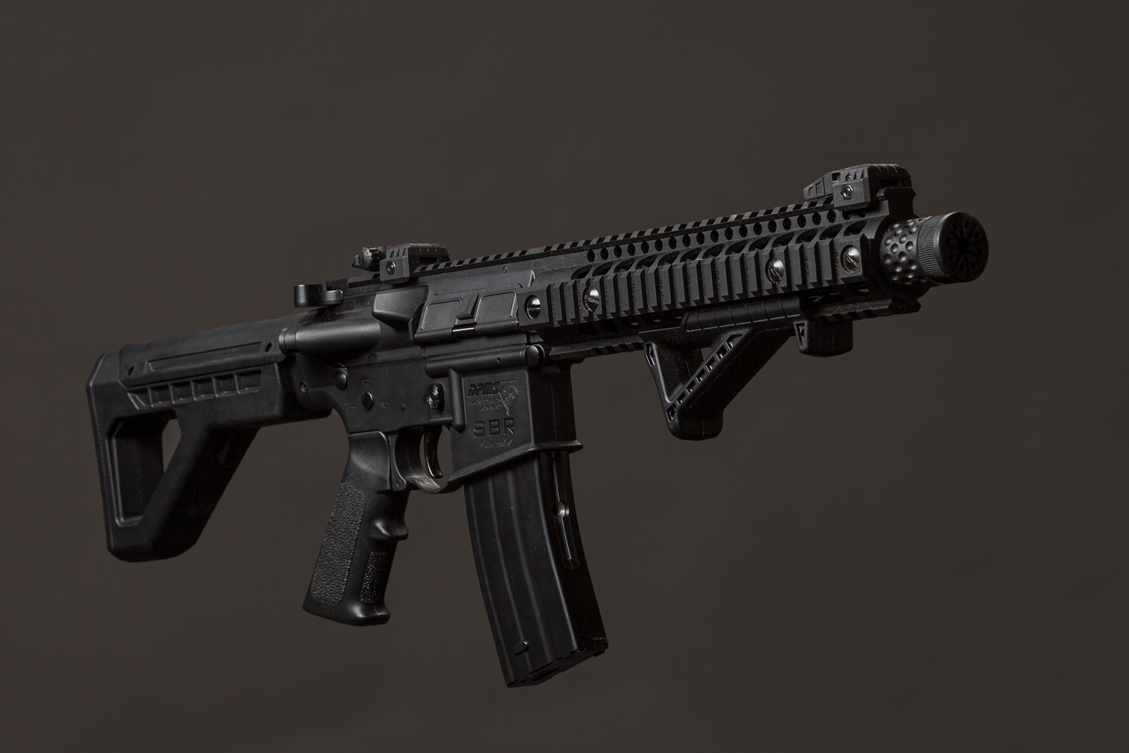 A black tactical rifle with a picatinny rail system and mounted optics, photographed against a grey background.
