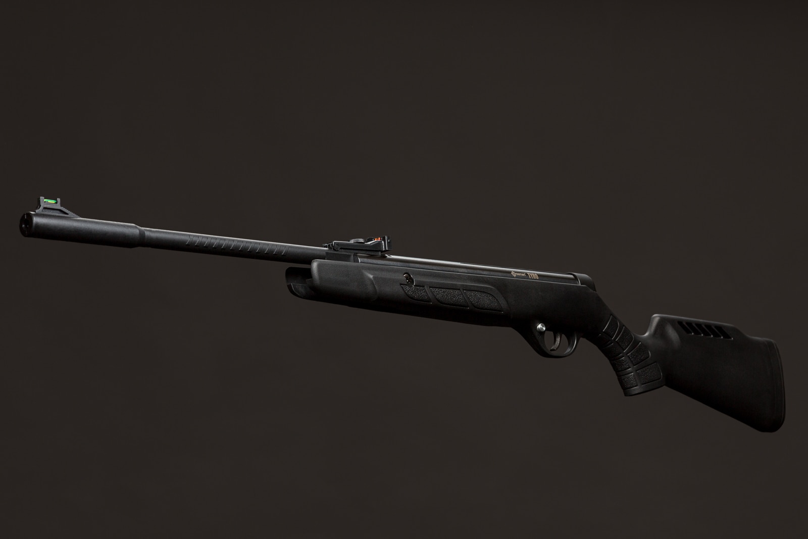 A black air rifle with a silencer and scope is displayed against a dark grey background.