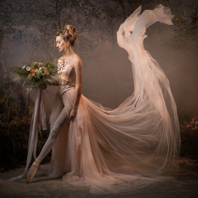 A ballet dancer in pointe shoes and flowing tulle gown holds a bridal bouquet against a textured studio backdrop.