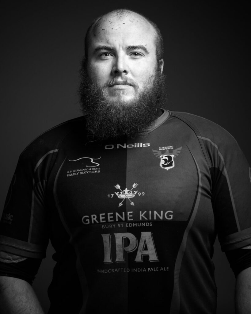 A bearded man wearing a black sports jersey with beer branding, photographed against a dark background in black and white.