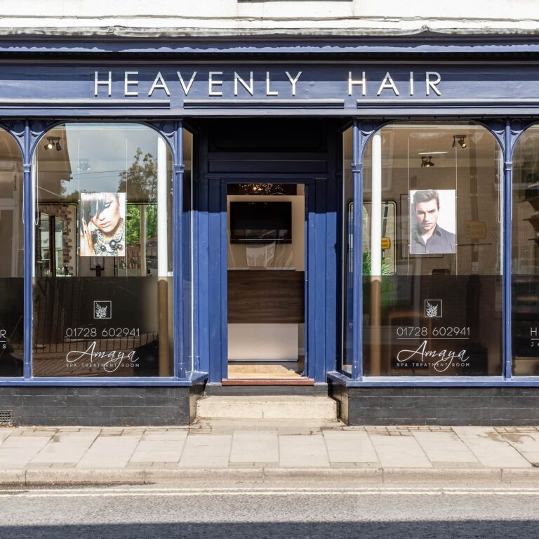 Storefront of Heavenly Hair salon with blue fascia, dark windows displaying headshots, and central entrance door.