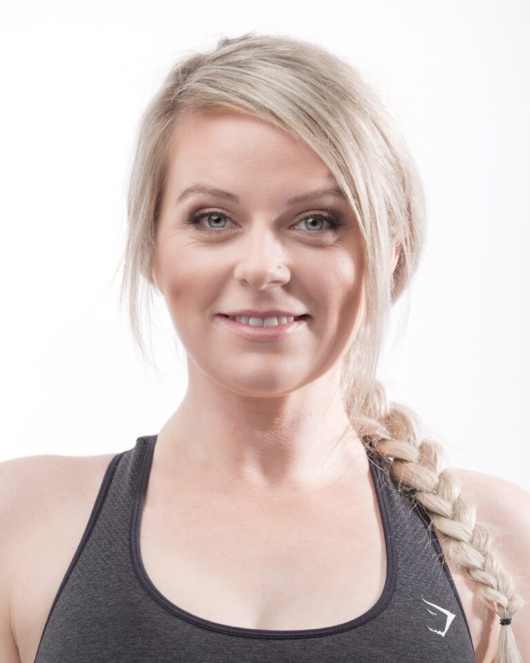 A woman with blonde hair in a braid wears a dark sports top and smiles at the camera against a white background.