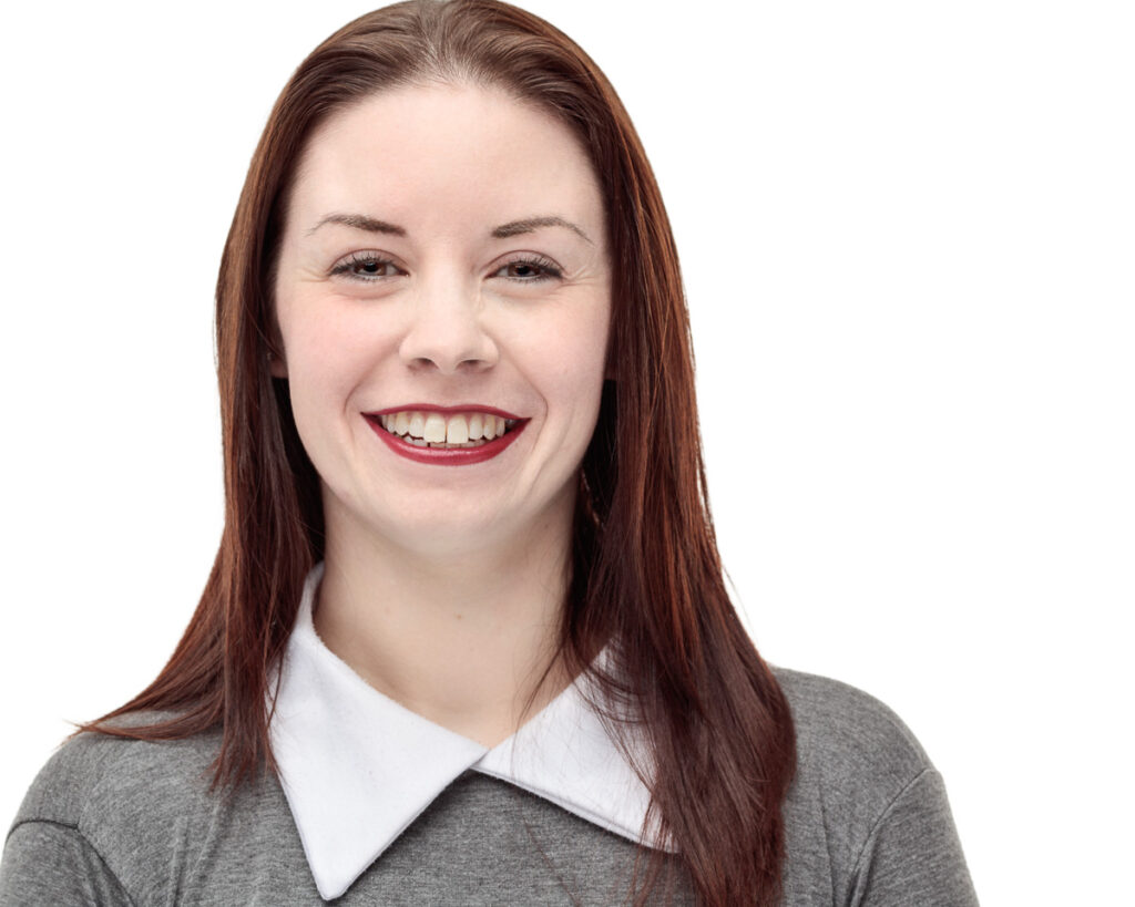 A woman with long reddish-brown hair and red lipstick smiles at the camera against a white background.