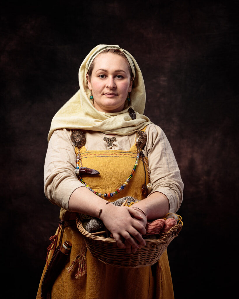 A woman wearing traditional Scandinavian folk costume stands against a dark background, holding a wicker basket.