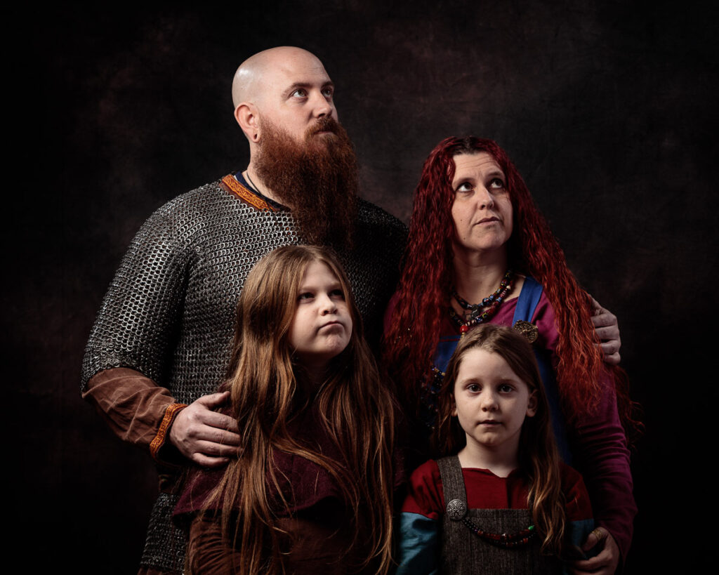 A family of four posed together against a dark background, dressed in medieval-style clothing with chainmail and tunics.