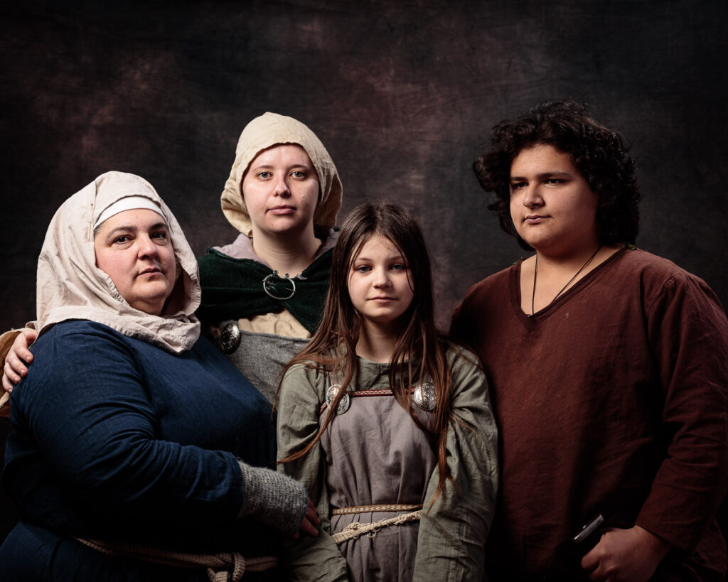 Four people in medieval-style clothing posed together against a dark textured background for a portrait photograph.