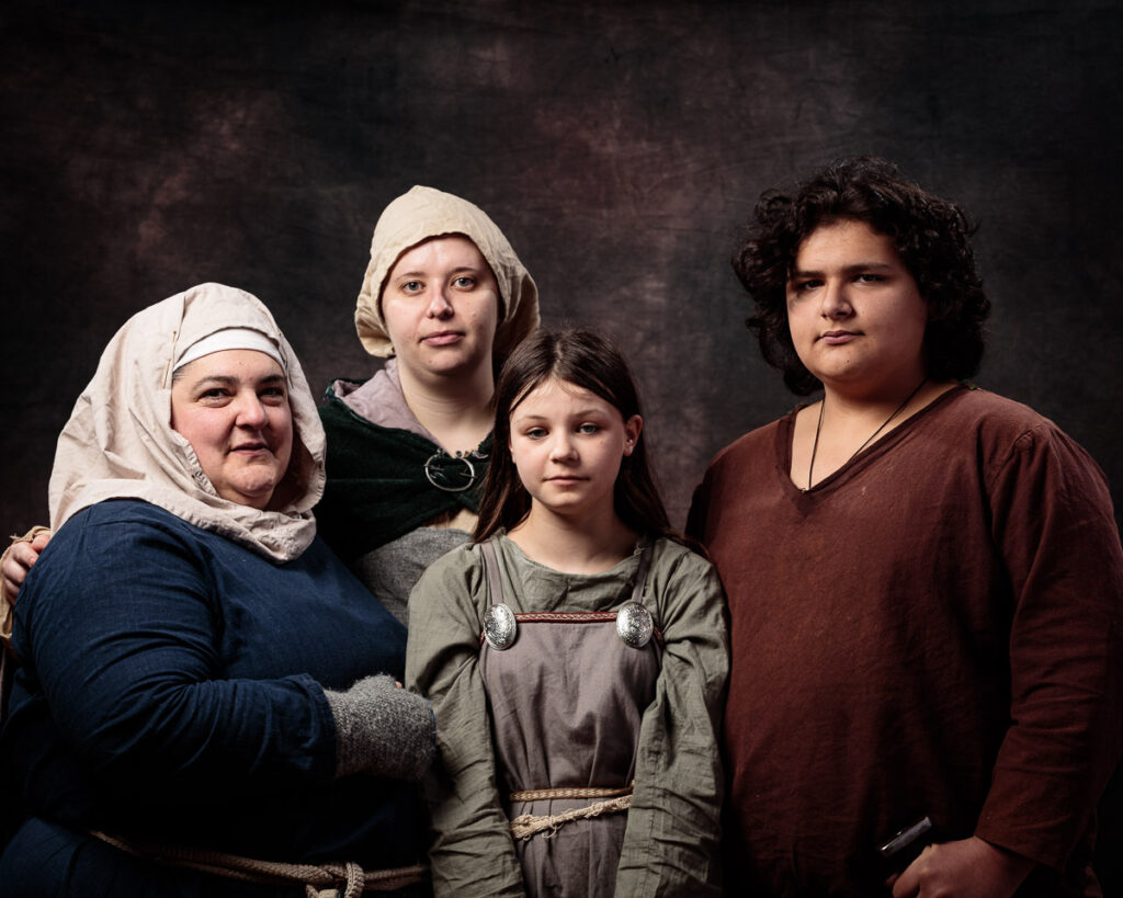 Four people in historical clothing pose together against a dark textured background for a formal portrait.
