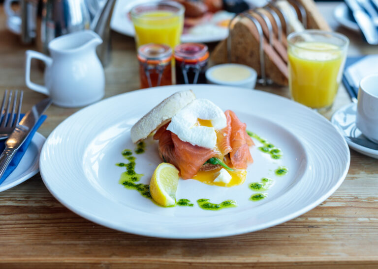 Smoked salmon and poached egg on white bread, garnished with green sauce and lime, served on a white plate at breakfast.