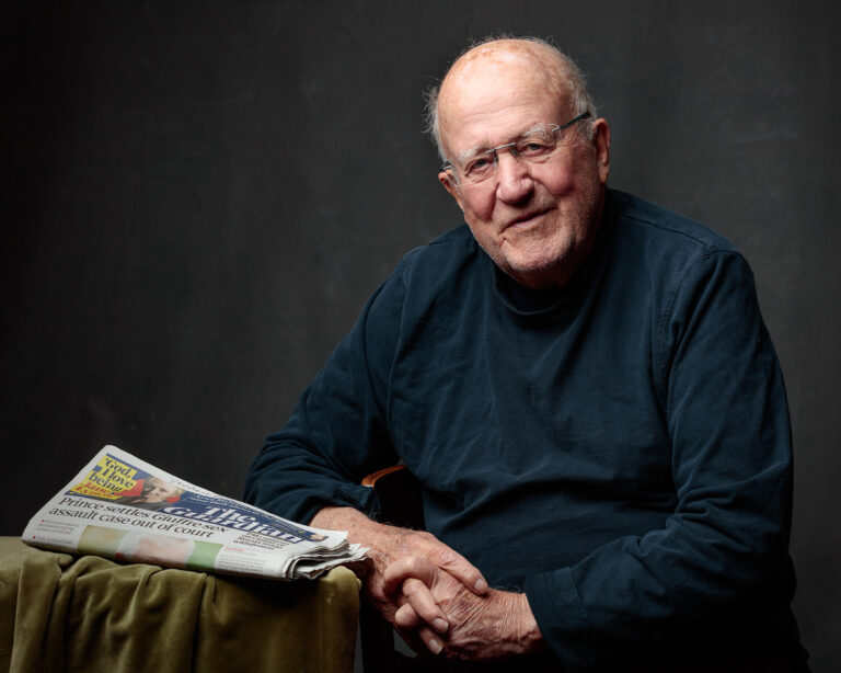 Portrait of an older man in a navy jumper with a newspaper on his knee