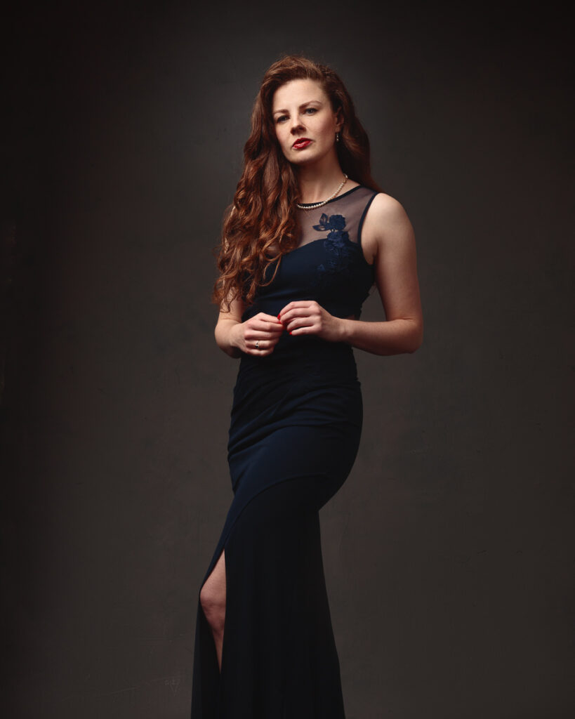 Full-length portrait of Isabelle in a navy lace-panel gown, dark background