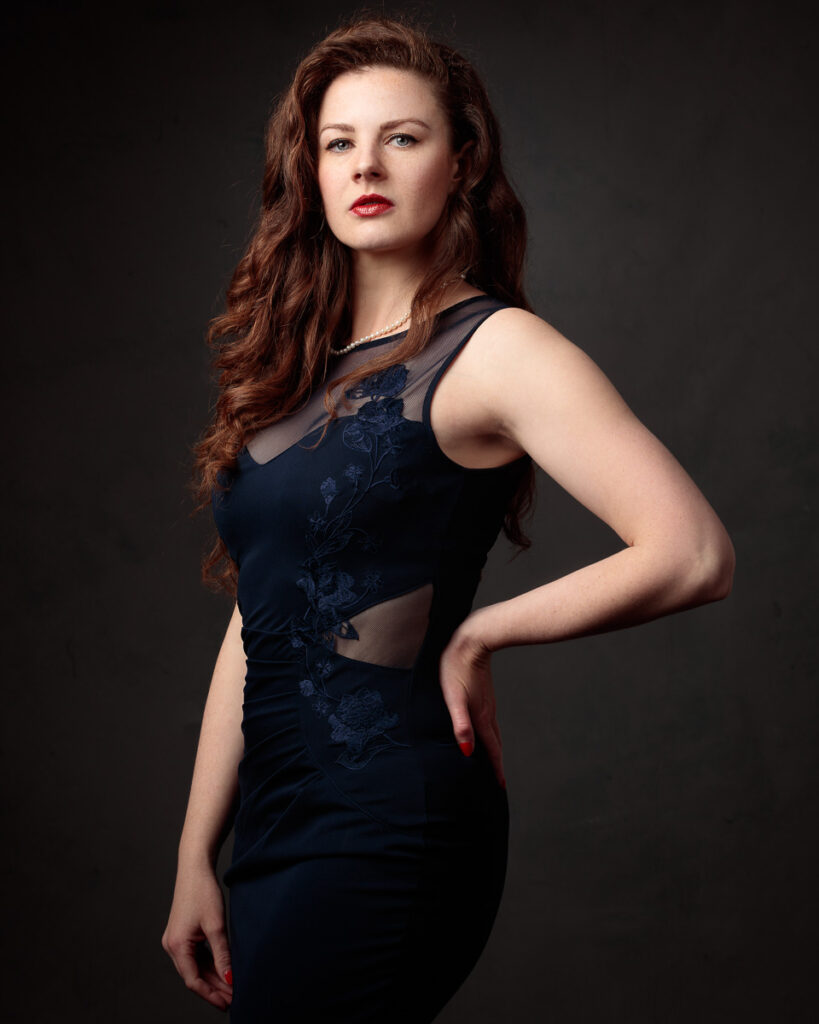 Full-length portrait of Isabelle in a navy lace-panel gown, hand on hip, dark background
