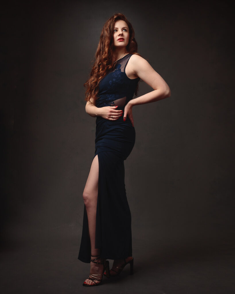 Full-length portrait of Isabelle in a navy lace-panel gown, strappy heels, dark background