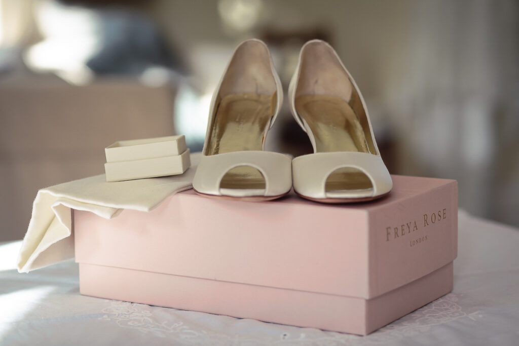 A pair of cream peep-toe heels sits on a pink Freya Rose shoebox with tissue paper, displayed indoors.