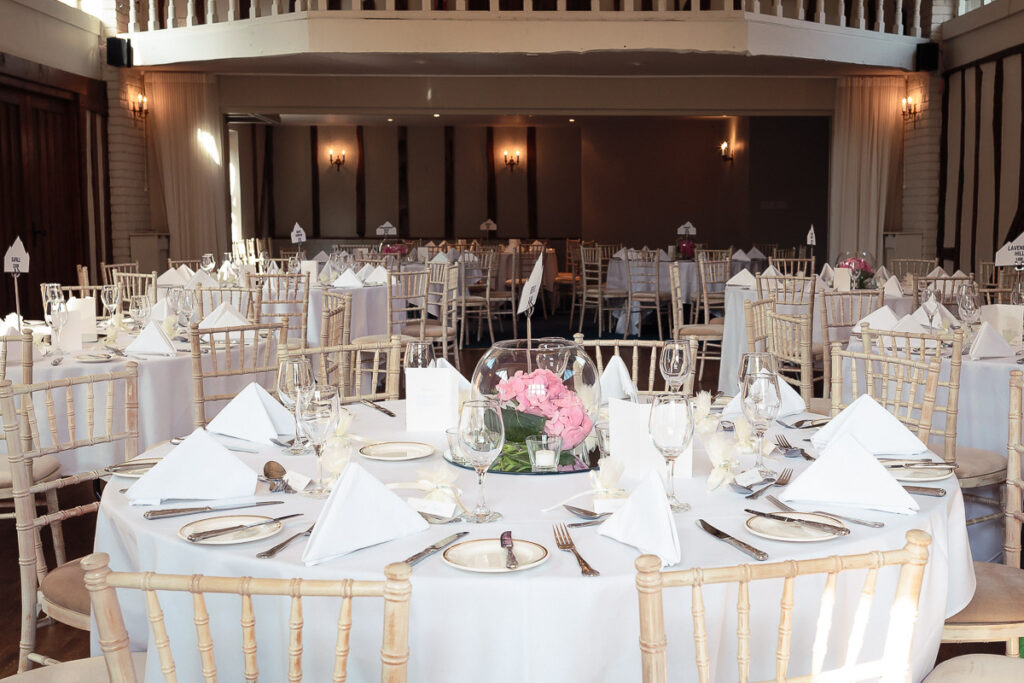 A formal banquet hall set up for a wedding reception with round tables, white linens, gold chairs, and pink floral centerpieces.