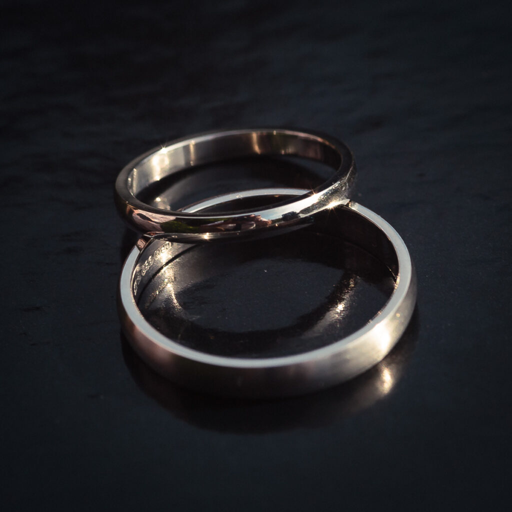 Two silver wedding rings placed together on a dark surface, catching light.