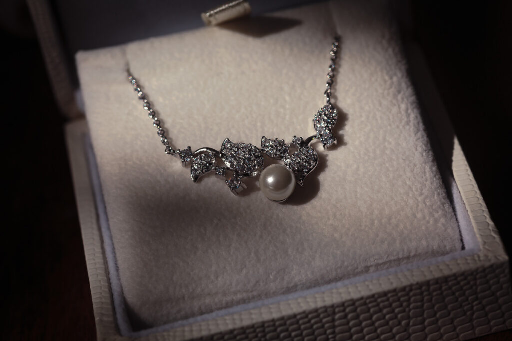 A silver necklace with three bow-shaped diamond pendants and a pearl centerpiece, displayed on a white velvet jewellery box.