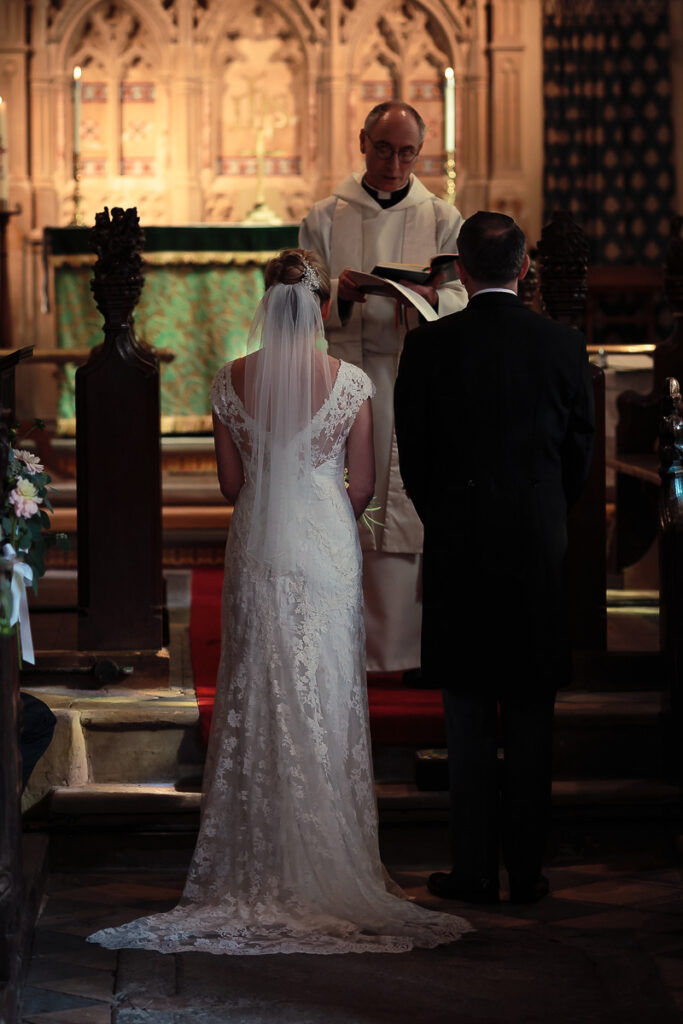 A bride and groom stand at the altar facing a priest during a wedding ceremony in a Gothic church interior.