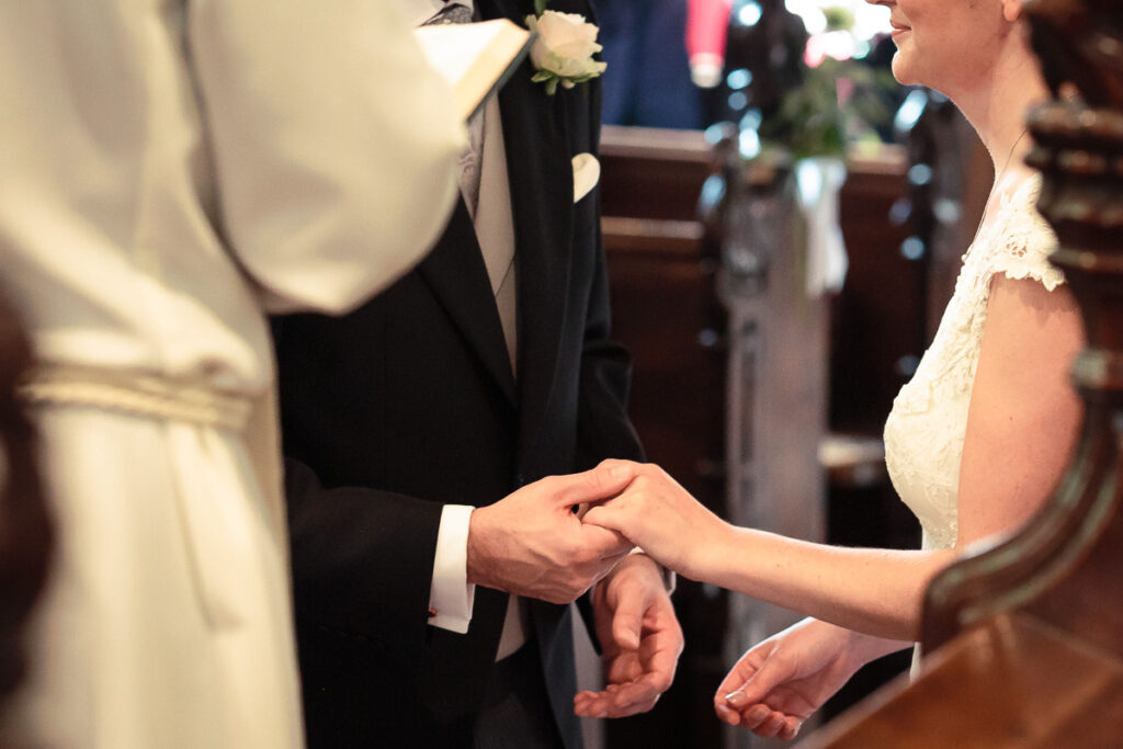 A bride and groom exchange rings during a wedding ceremony in a church, holding hands at the altar.