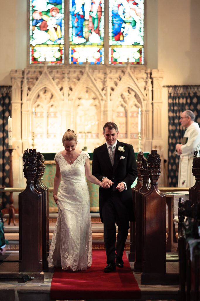 A bride and groom walk together down the aisle of a grand church with stained glass windows and ornate stonework during their wedding ceremony.