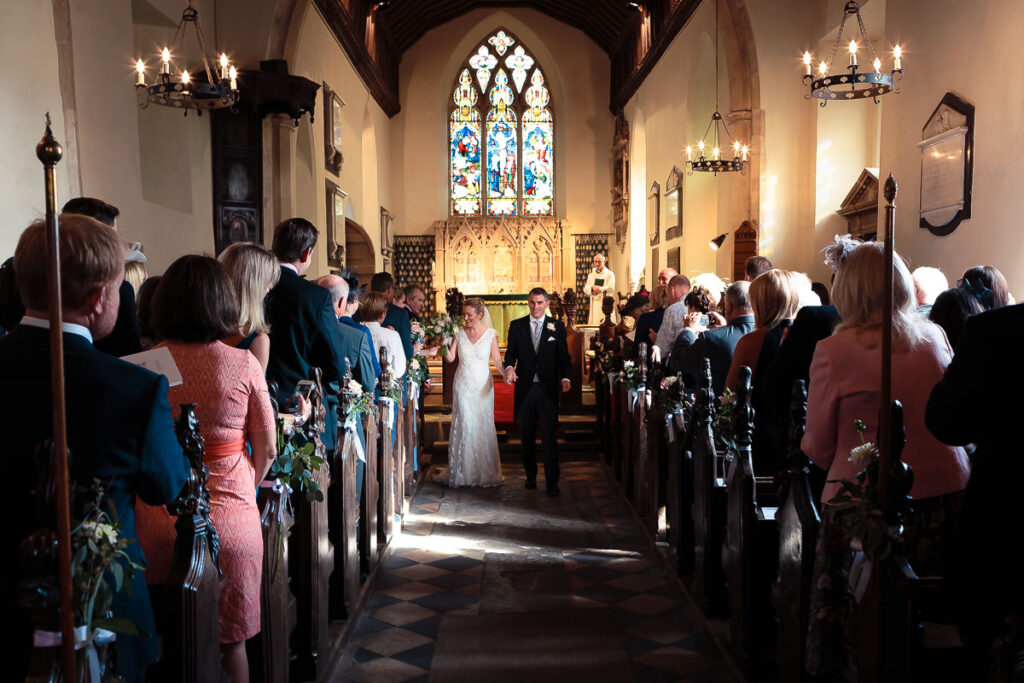 A wedding ceremony in a church, with the bride and groom standing at the altar while guests sit in pews on either side.