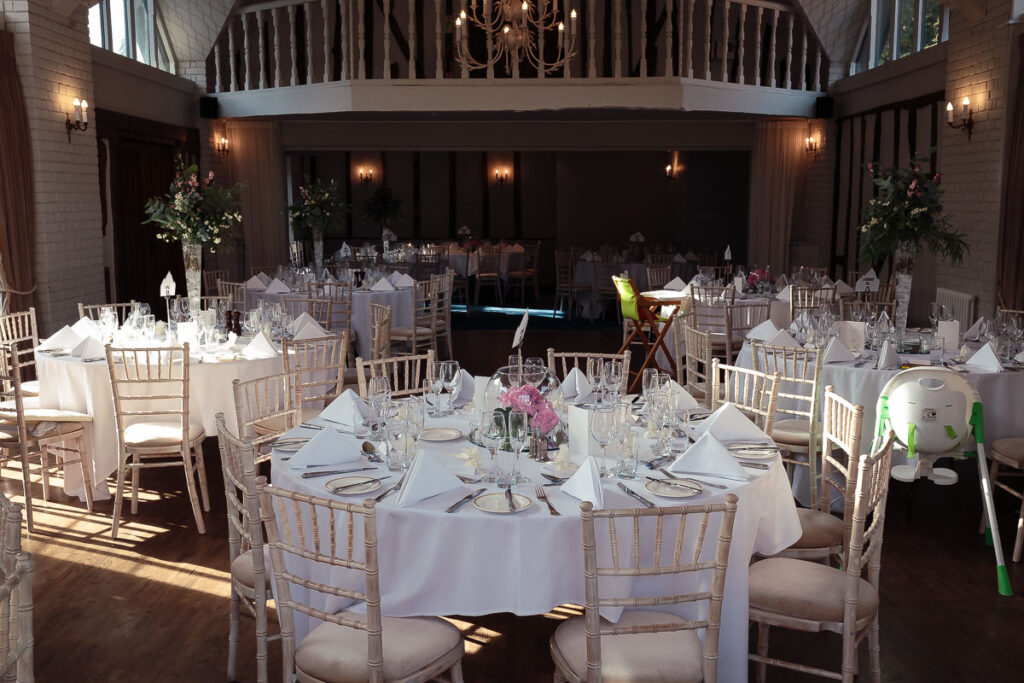 An elegant wedding reception venue with round tables dressed in white linens, chiavari chairs, place settings, and floral centrepieces.