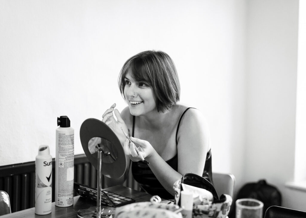 Black and white personal branding photograph of a woman applying make-up at a mirror
