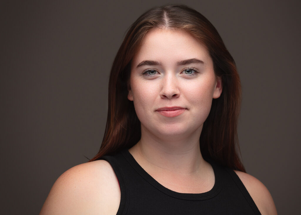 Woman with long hair, black top, neutral background.