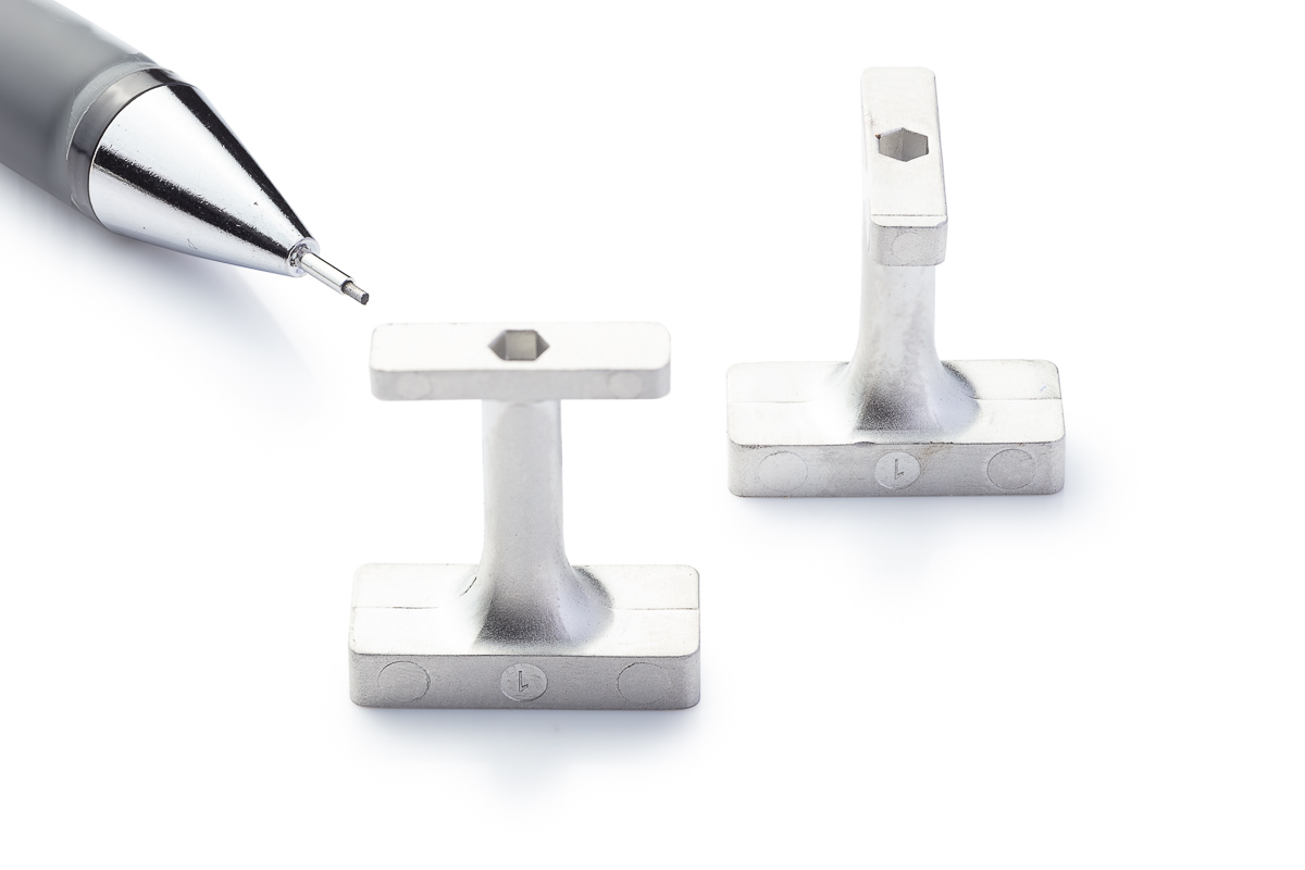 A second view of the two stainless steel T section brackets, one upright and one angled away, with a pencil tip for scale.