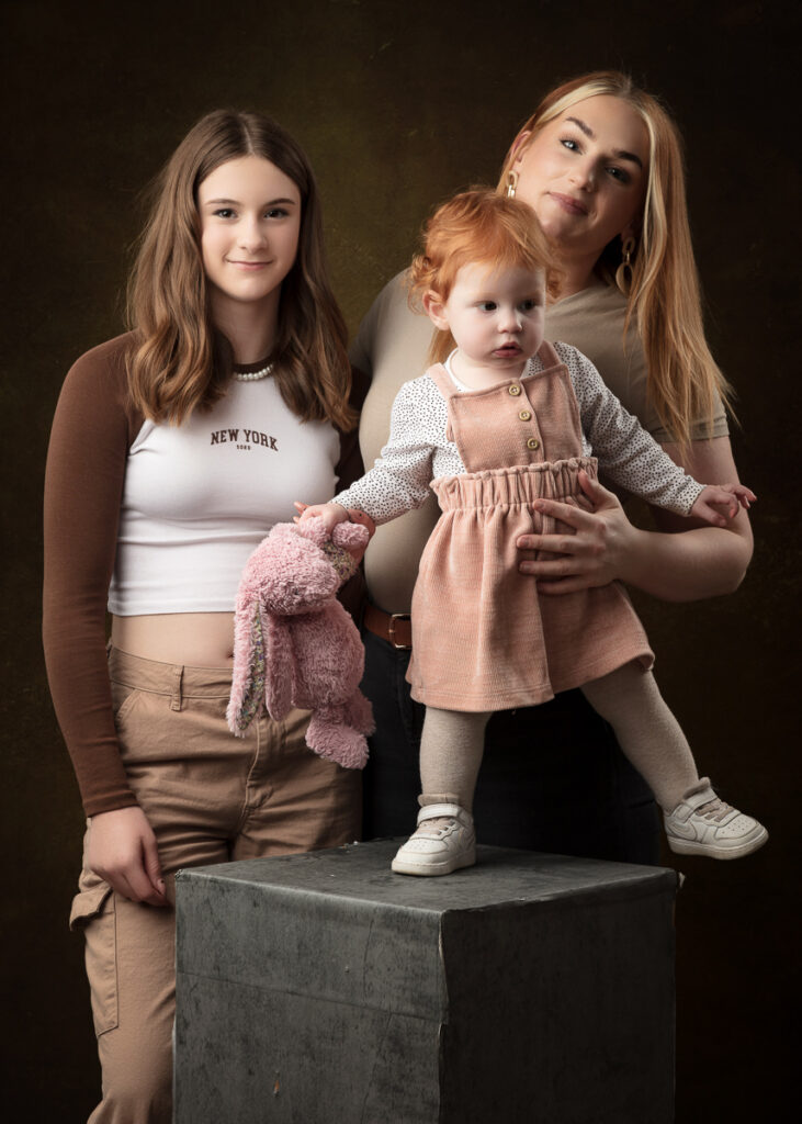 Studio family portrait with a toddler standing on a wooden block, against a dark backdrop