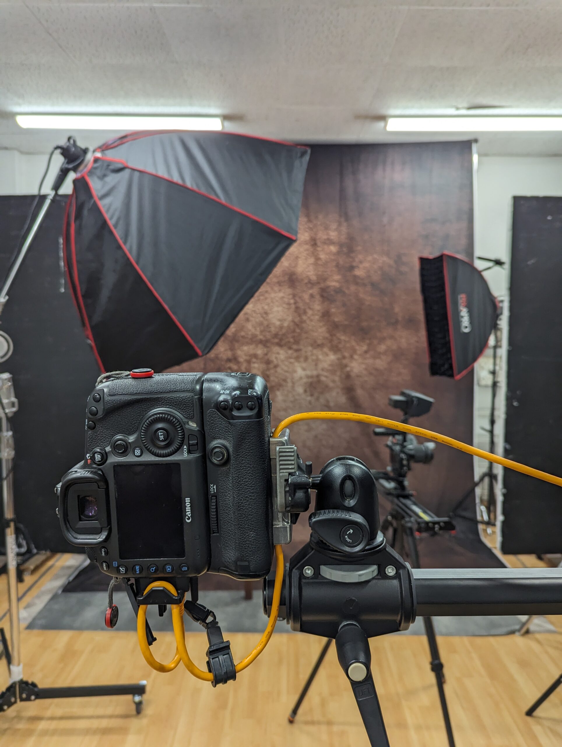 Camera on a tripod in the studio, facing a mottled brown backdrop lit by softboxes