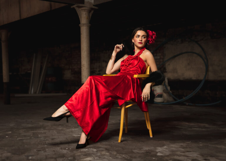 Portrait of a woman in a red dress and flower hair clip seated in an old industrial building in Halesworth