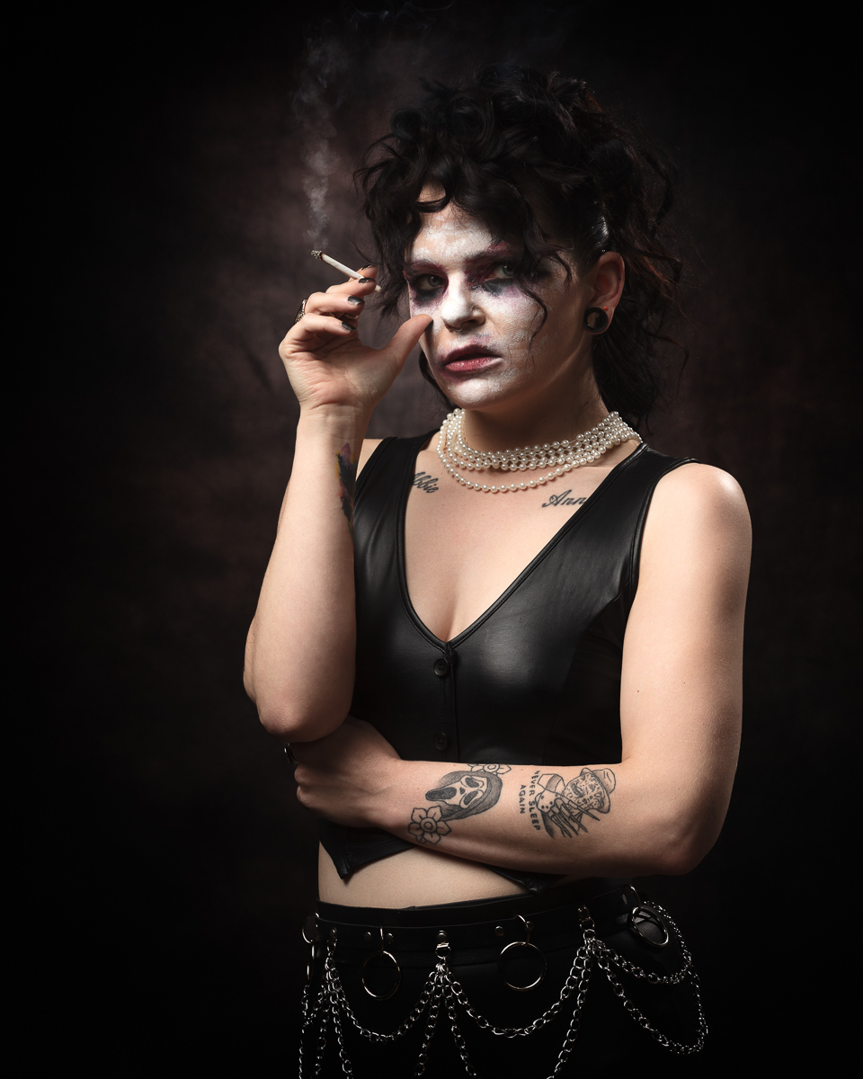 Person in gothic makeup smoking, wearing leather top.