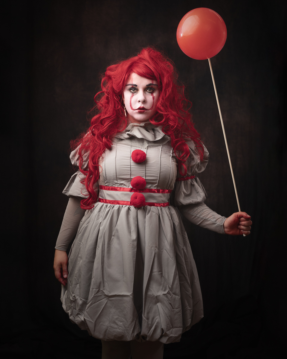 Person dressed as a clown holding a red balloon.