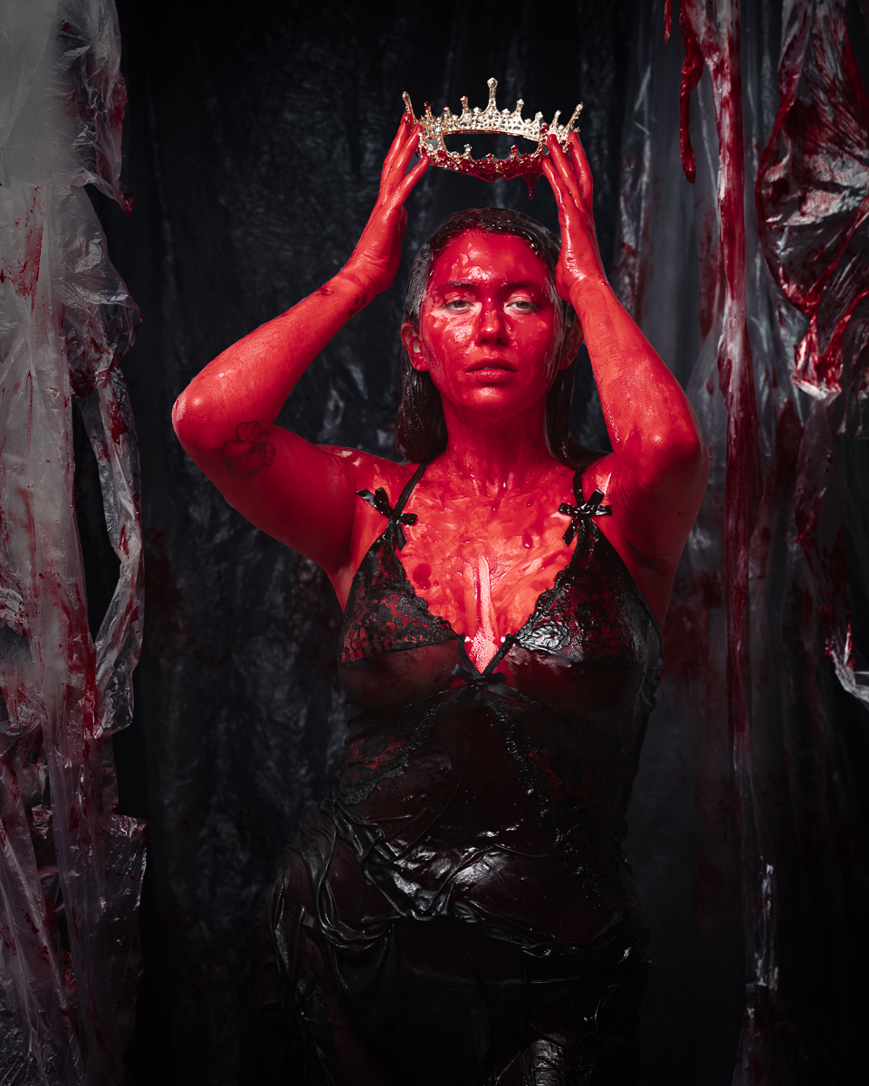 Person covered in red paint holds a crown.