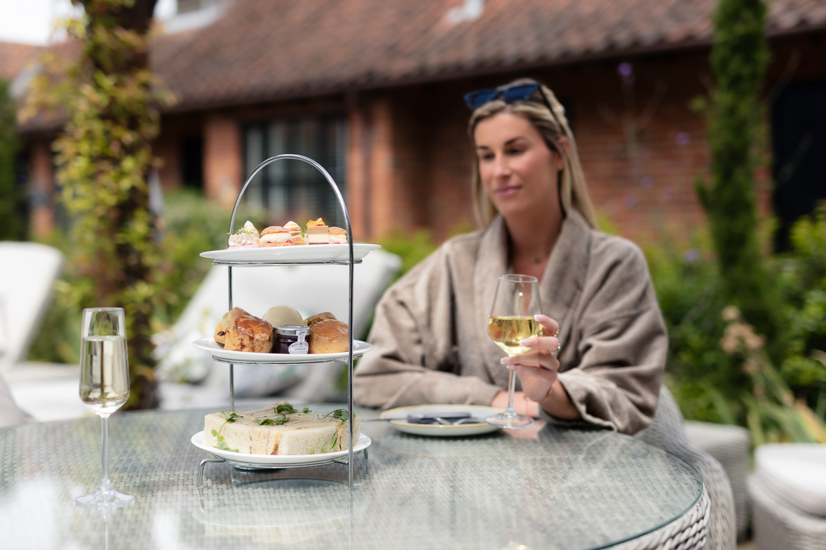 Woman enjoying afternoon tea and a glass of wine on the terrace at Seckford Hall