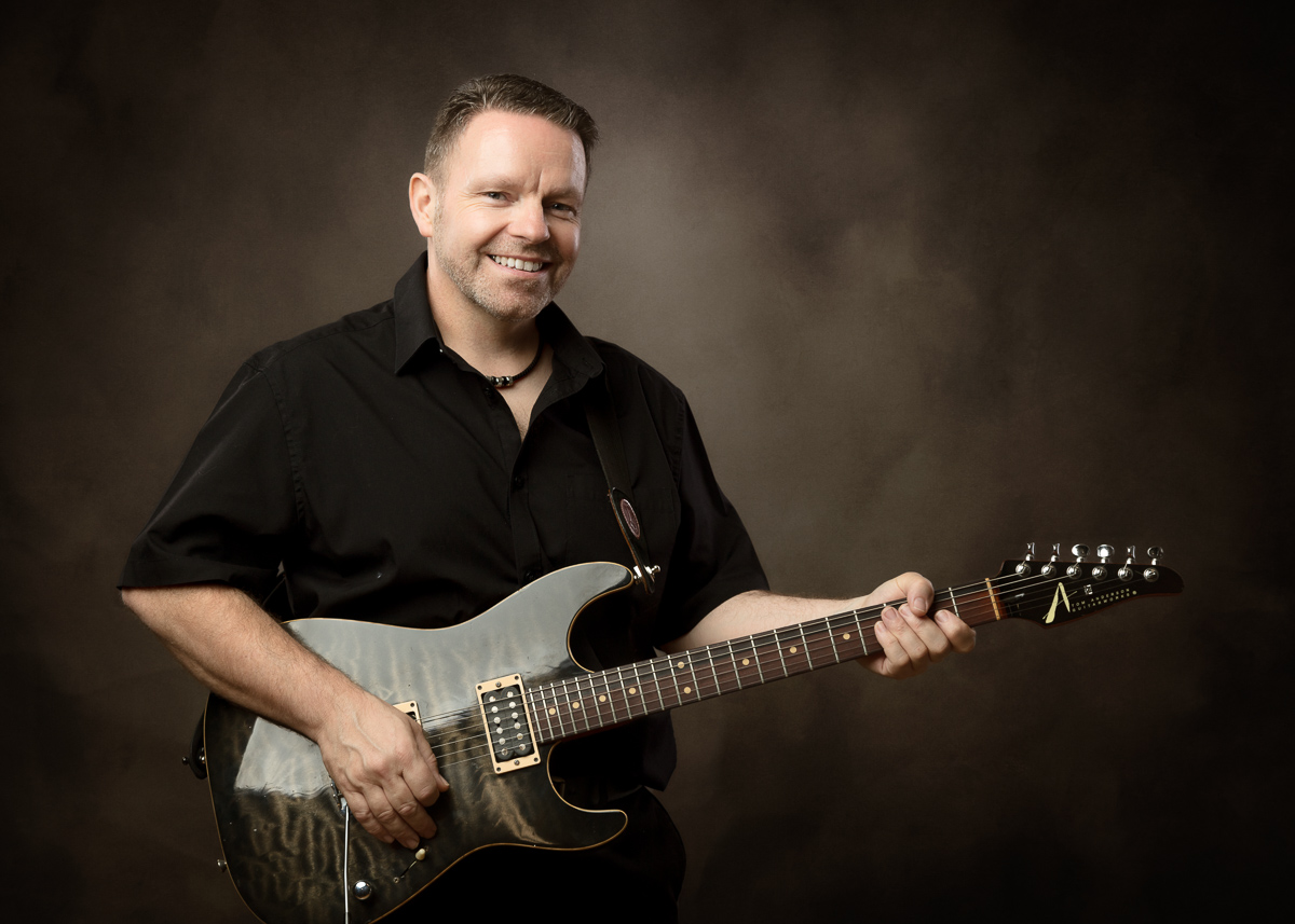 Smiling man playing electric guitar wearing black shirt