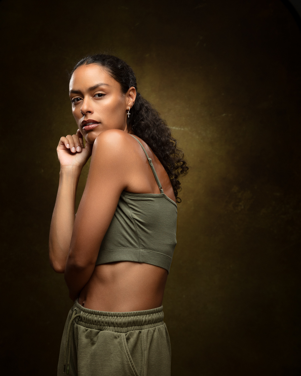 Woman in olive sports top posing against brown backdrop