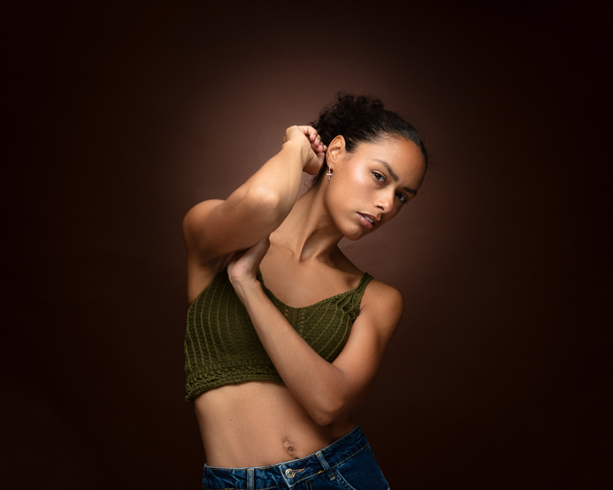 Woman in olive crop top and jeans against brown background