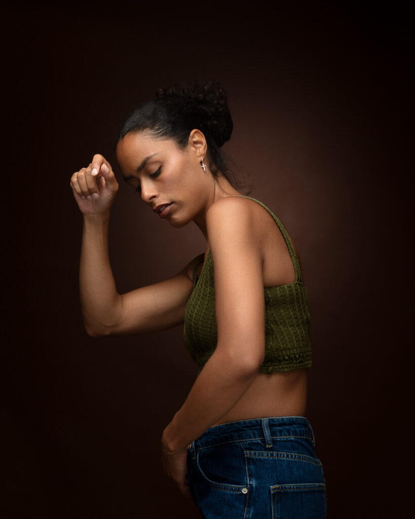 Woman in green top and jeans posing against dark background