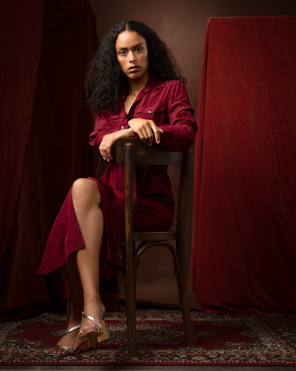 Woman in burgundy shirt seated on wooden chair, studio portrait