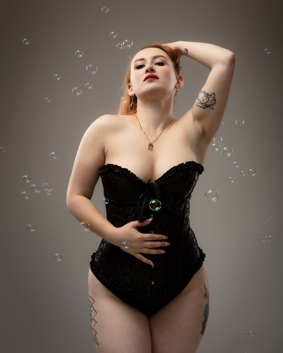 Woman in black corset with red hair surrounded by soap bubbles