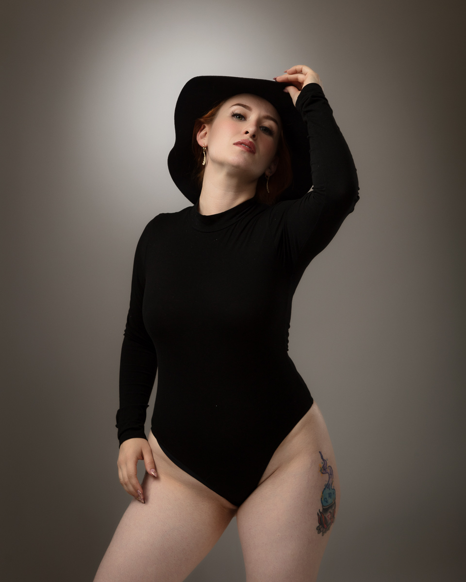 Woman in black bodysuit and hat against grey background