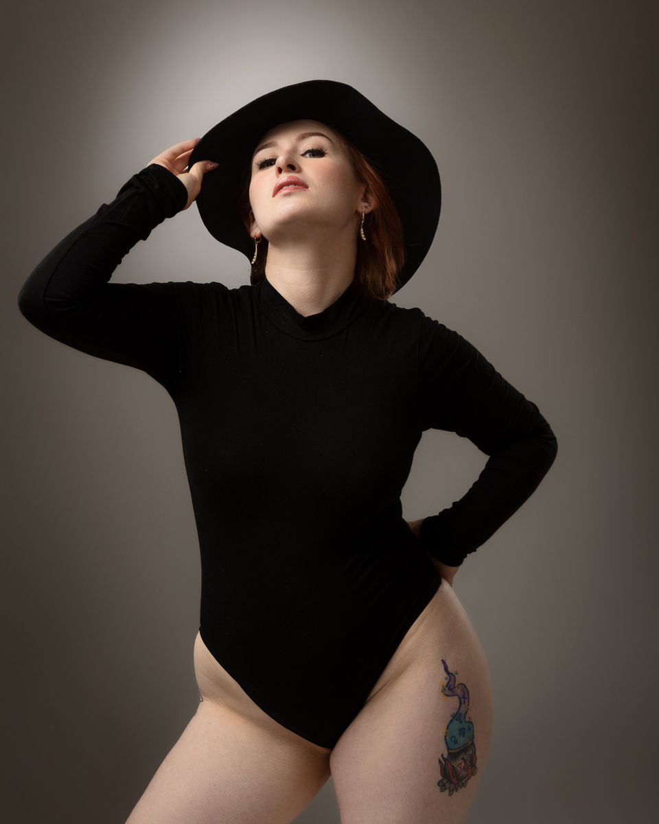 Woman in black bodysuit and wide-brimmed hat posing