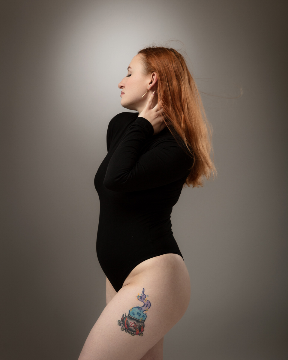 Woman with red hair and visible thigh tattoo posing in profile