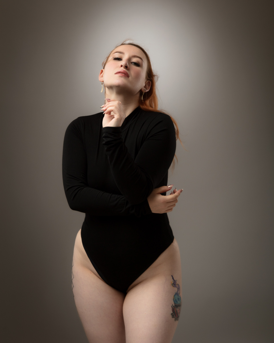 Woman in black bodysuit posing thoughtfully against grey background
