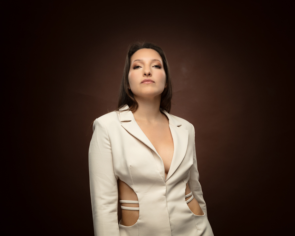 Woman wearing cream blazer with cutout details against brown background
