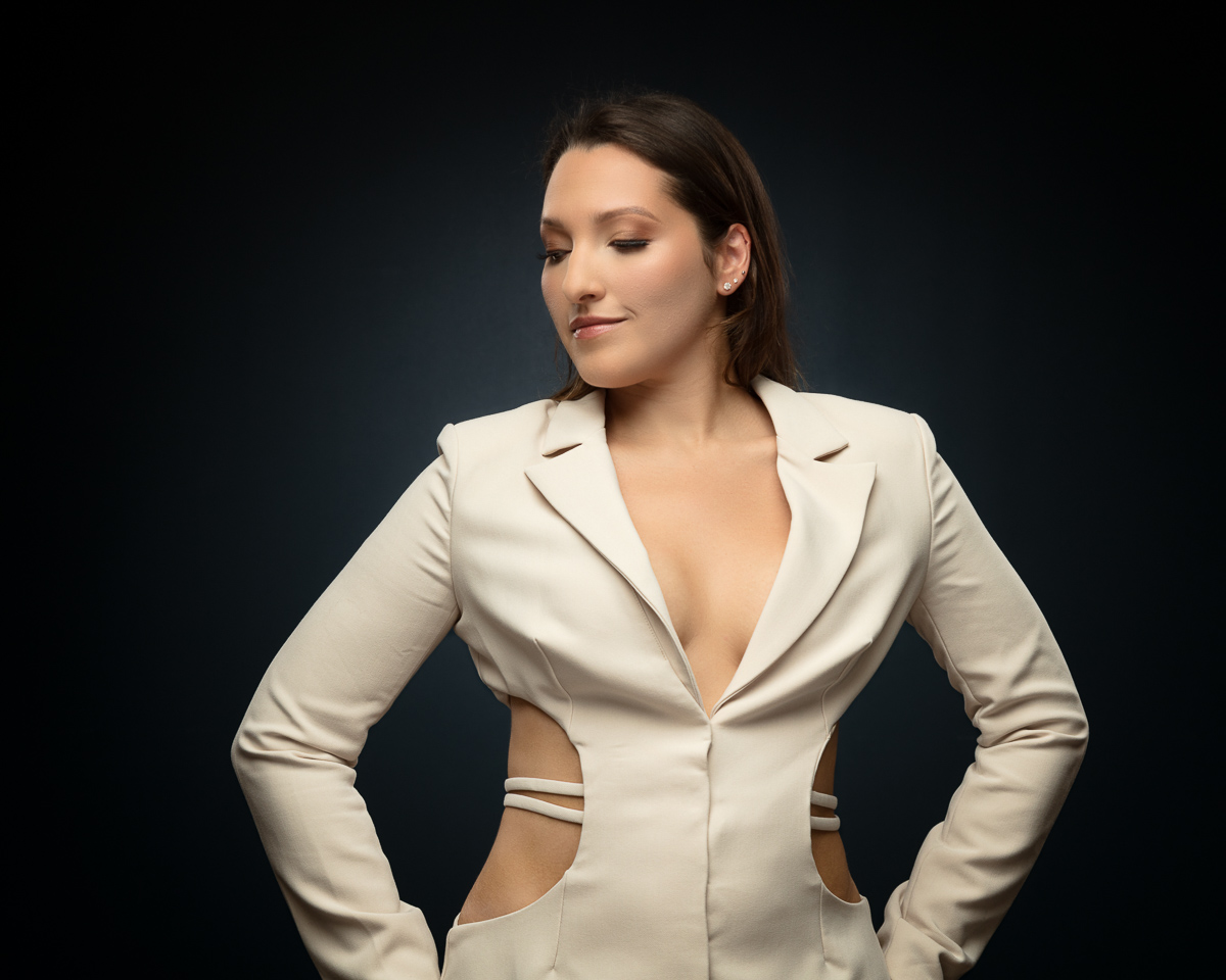 Woman wearing cream blazer with cutout details, dark background